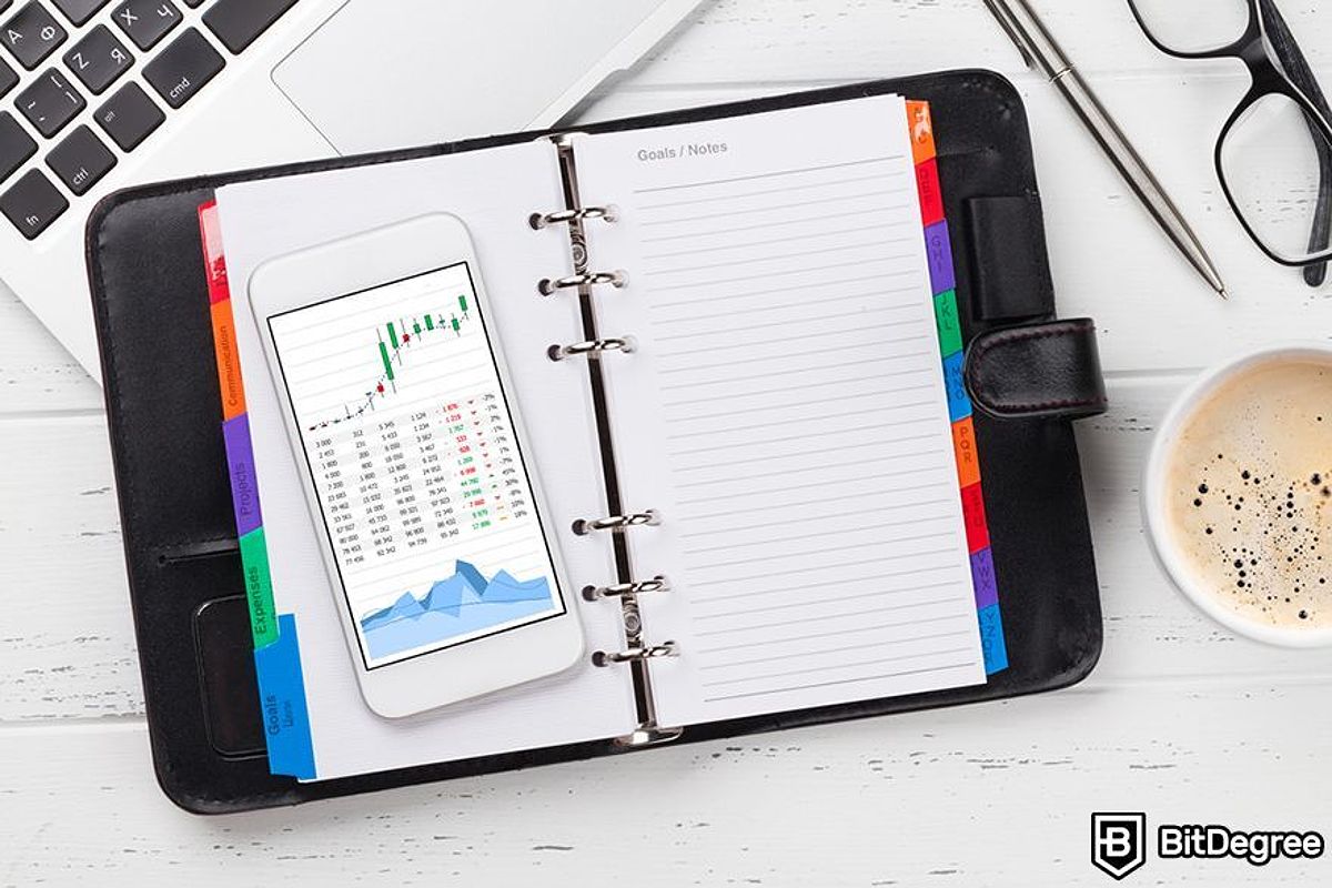 A notepad and a phone with a trading chart