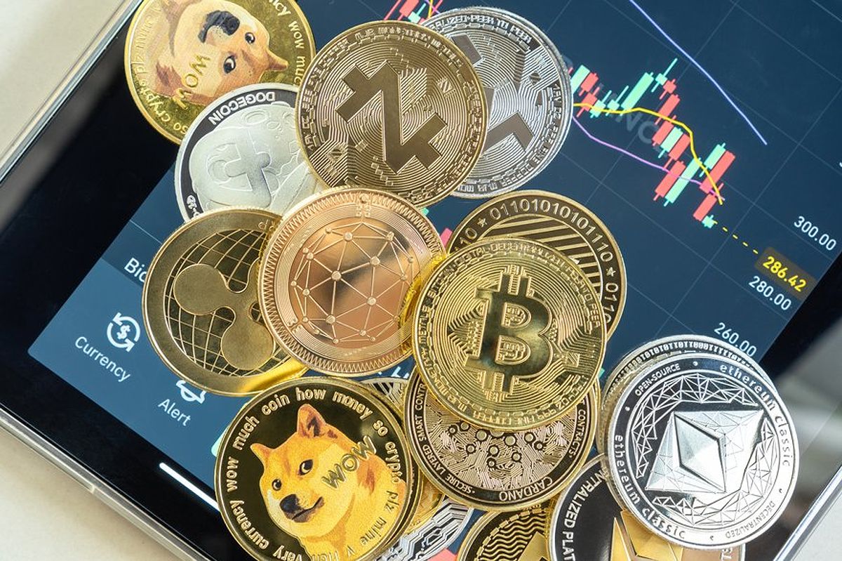 Different cryptocurrencies lying in a pile atop a smartphone opened to a trading app